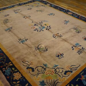 A beige rug with stylized multicolored floral sprigs and a wide navy and gold border on wooden floors.