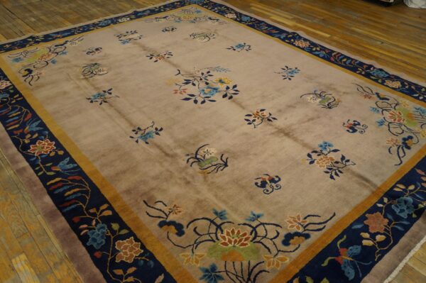 A beige rug with stylized multicolored floral sprigs and a wide navy and gold border on wooden floors.