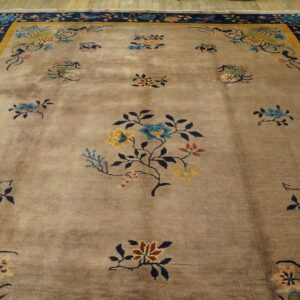 Low-pile tan rug with colorful floral sprays and a navy border, displayed on hardwood flooring.