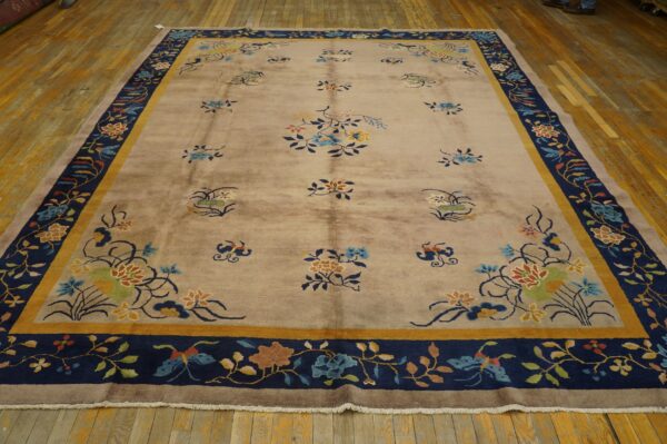 Beige rug with multicolored scattered florals and a wide navy and gold patterned border on wood floor.