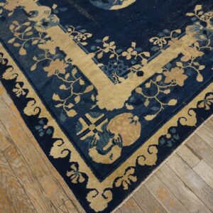 Corner of a navy blue and gold floral rug with a decorative border on distressed plank wood flooring.