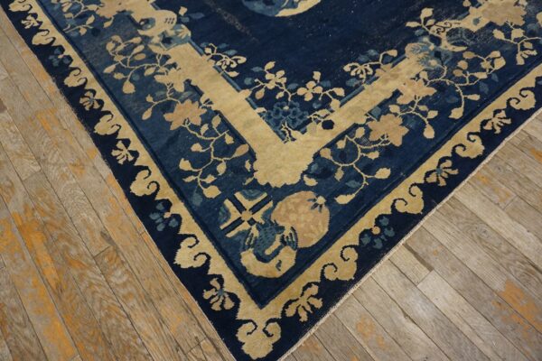 Corner of a navy blue and gold floral rug with a decorative border on distressed plank wood flooring.