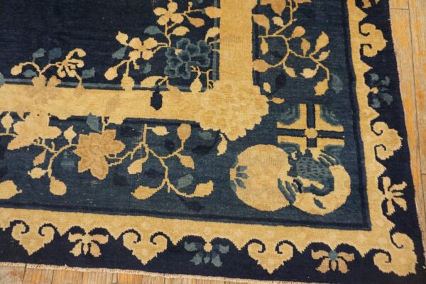 A close-up view shows a low-pile rug with navy blue, goldenrod, and teal floral patterns over wood flooring.