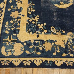 Close-up of a distressed navy and gold rug featuring a detailed floral border on rustic wood flooring.