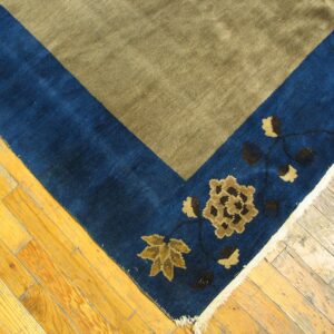 Khaki field rug with a wide blue border featuring gold and brown floral designs on plank flooring.