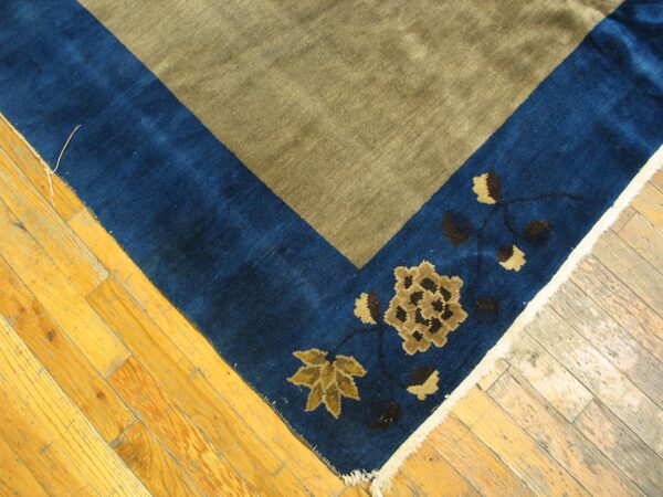 Khaki field rug with a wide blue border featuring gold and brown floral designs on plank flooring.