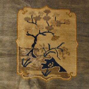 Tan medallion featuring a dark blue and brown stylized tree pattern on a muted grayish-brown rug.