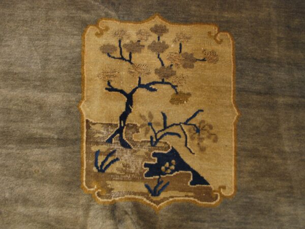 Tan medallion featuring a dark blue and brown stylized tree pattern on a muted grayish-brown rug.