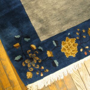 Blue border with gold and teal floral motifs meets a gray field, resting on light wood floor.