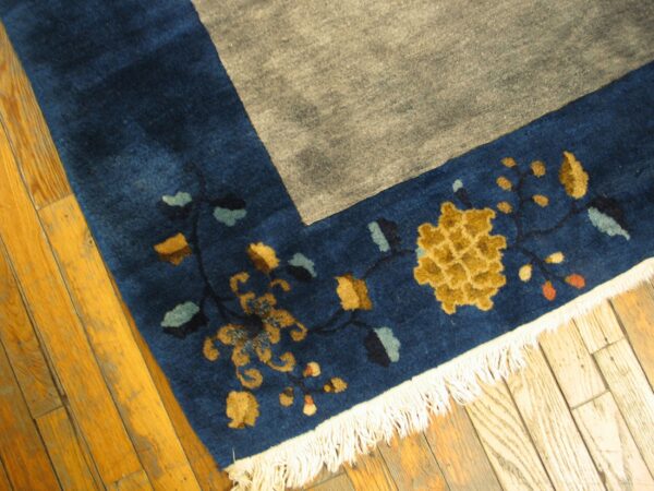 Blue border with gold and teal floral motifs meets a gray field, resting on light wood floor.