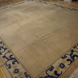 Lustrous beige rug with a wide blue scroll pattern border lying on distressed wood floors.