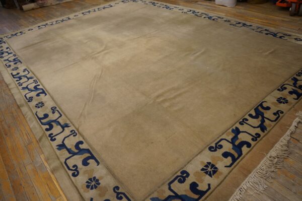 Lustrous beige rug with a wide blue scroll pattern border lying on distressed wood floors.