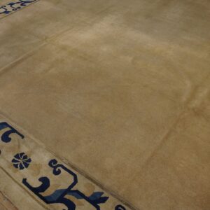 Tan field rug with a detailed navy blue and light beige geometric border on wood planks.