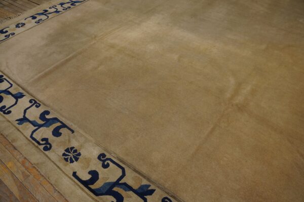 Tan field rug with a detailed navy blue and light beige geometric border on wood planks.