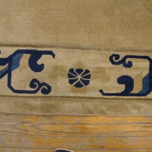 Beige rug border featuring navy and light blue scroll motifs rests on distressed wood plank flooring.