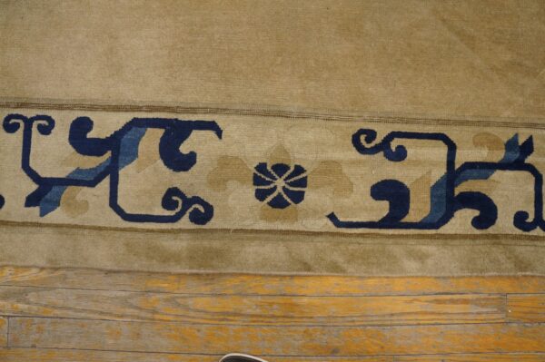 Beige rug border featuring navy and light blue scroll motifs rests on distressed wood plank flooring.