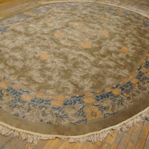 Round olive and tan rug with bright blue and apricot floral borders on distressed wood floors.