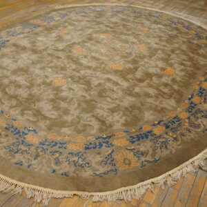 Round olive green rug with cloud patterns and a blue and salmon floral border on worn wooden floorboards.