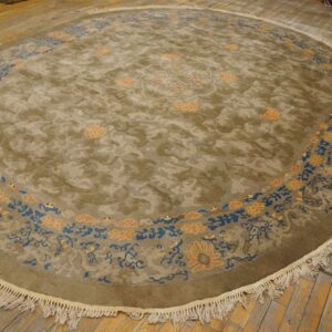 Circular olive rug with tone-on-tone cloud pattern, blue and peach floral border, and prominent white fringes.