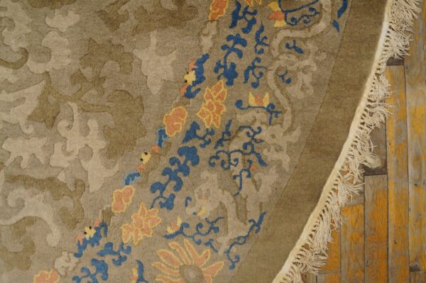 Muted brown rug detail showing carved floral patterns, blue vines, and peach flowers, resting on distressed wooden floors.