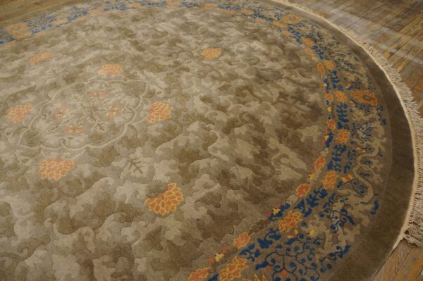 Round, taupe rug featuring carved botanical patterns and a border with blue and orange floral accents on hardwood floors.