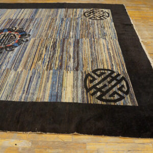 Textured rug featuring vertical blue, brown, and beige stripes with a black border and stylized corner motifs.