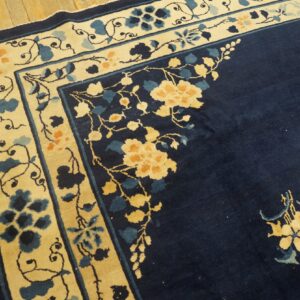 Navy blue rug with a cream border featuring yellow and blue floral motifs rests on wood plank flooring.