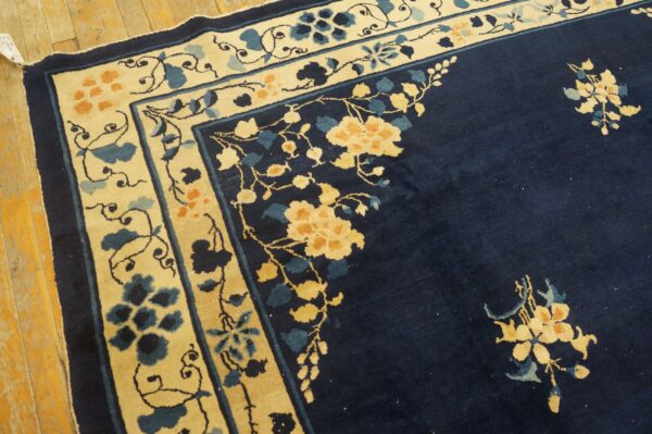Navy blue rug with a cream border featuring yellow and blue floral motifs rests on wood plank flooring.