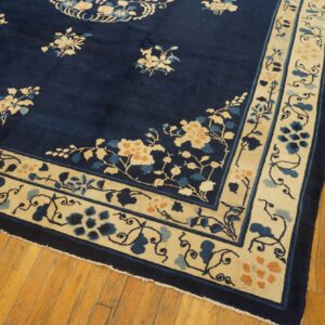 Deep blue floral rug featuring light cream borders with blue and orange vine motifs on wood flooring.