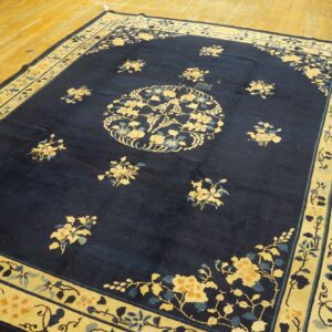 A dark blue rug with contrasting cream and gold floral border and medallions rests on light wood floors.