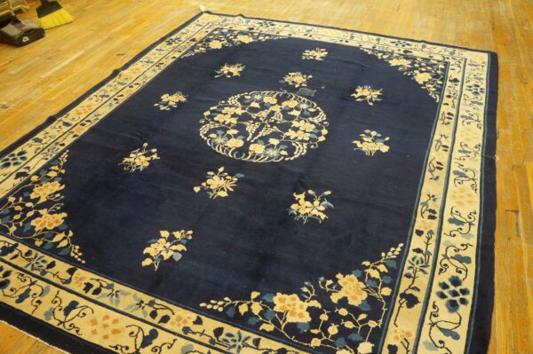 A dark blue rug with contrasting cream and gold floral border and medallions rests on light wood floors.