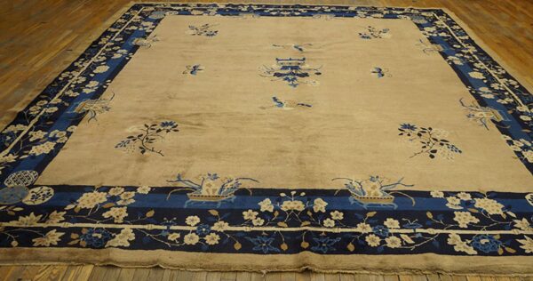 Large tan rug with dark blue borders and scattered blue and cream floral motifs on wood flooring.
