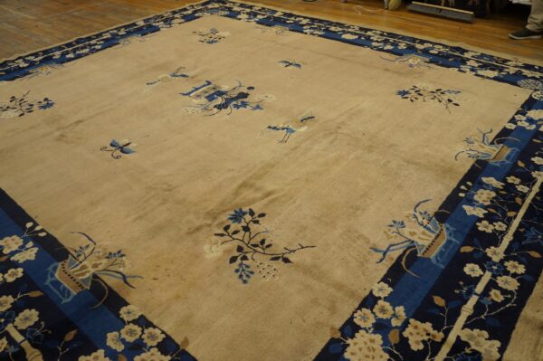 Beige rug with scattered blue motifs and a wide navy border, shown on a wood plank floor.