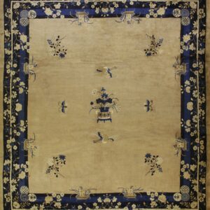 Square beige rug with a detailed navy blue floral border and a central design of a vase and birds.