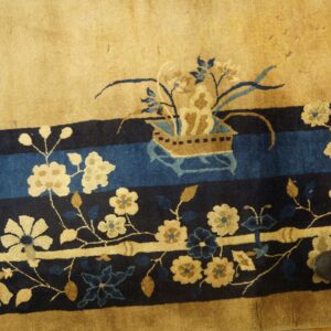 High-pile rug in tan and deep blue features detailed floral borders resting on distressed wood flooring.