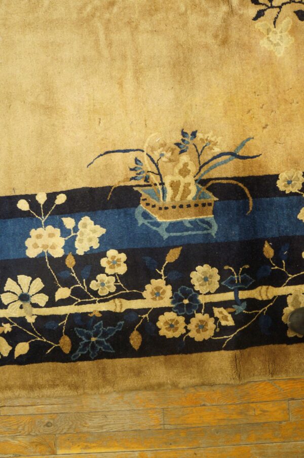 High-pile rug in tan and deep blue features detailed floral borders resting on distressed wood flooring.