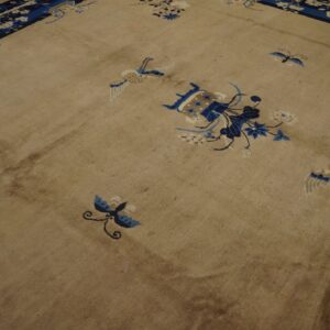 Tan rug featuring blue and white scatter floral and bird motifs rests on wood plank flooring.