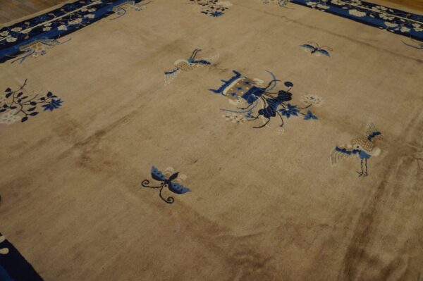 Tan rug featuring blue and white scatter floral and bird motifs rests on wood plank flooring.