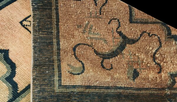 Detailed view of a tan rug corner, showing blue floral motifs, a striped border, and a pink folded edge.