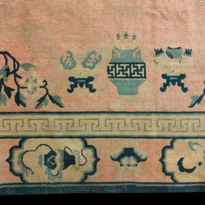 Low-pile rug detail showing a pink field with teal vase motifs, floral vines, and geometric borders.