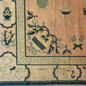 Muted salmon rug corner showing a pattern of vases and florals bordered by a Greek key band.