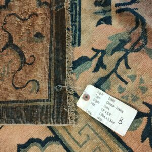 Muted peach rug with dark teal floral designs, showing the texture, visible fringe, and an attached sales tag.
