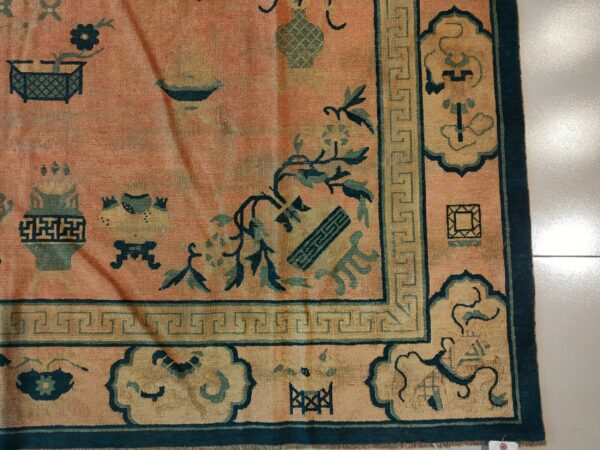 Salmon rug with teal oriental motifs, a yellow cartouche border, and a greek key design.