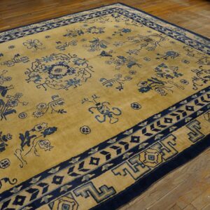 A golden yellow rug with scattered navy blue motifs and layered borders rests on wooden planks.