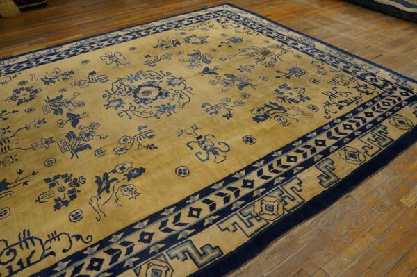 A golden yellow rug with scattered navy blue motifs and layered borders rests on wooden planks.