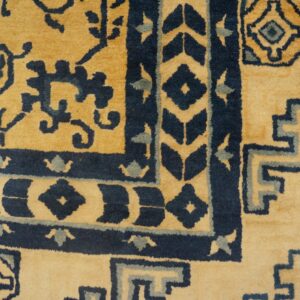 Corner of a gold and dark blue patterned rug showing geometric borders next to distressed wood flooring.