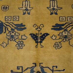 Gold pile rug featuring dark blue decorative symbols, geometric designs, and a central butterfly motif.