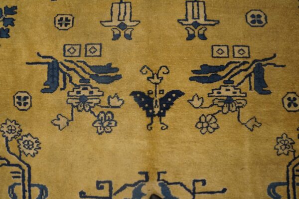 Gold pile rug featuring dark blue decorative symbols, geometric designs, and a central butterfly motif.