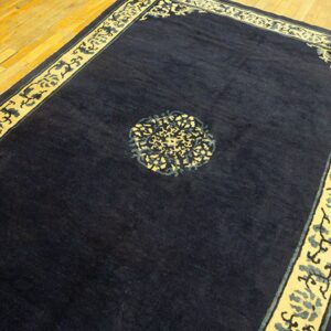 Rectangular dark blue rug with yellow and blue decorative borders on polished wood planks.