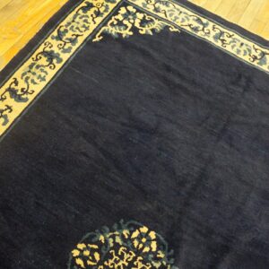 Dark blue rug with a yellow and teal scroll border rests on shiny golden hardwood floors.